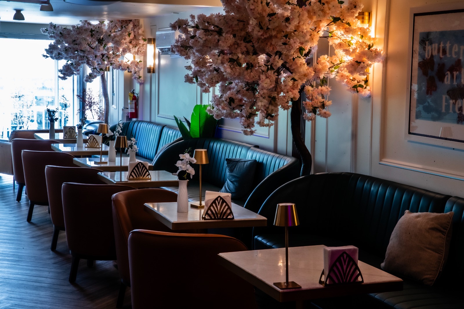 The Long Room — Teal Banquettes Long teal banquette and tan chairs beneath blossom trees at Yorkville Lounge