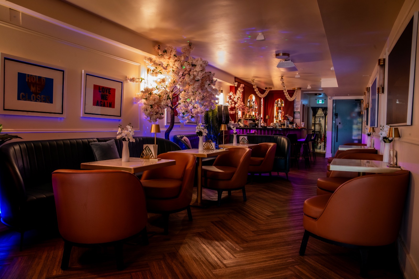 Love Me Again — Lounge View to the Bar Lounge view toward the bar with Love Me Again pop-art prints and blossom tree